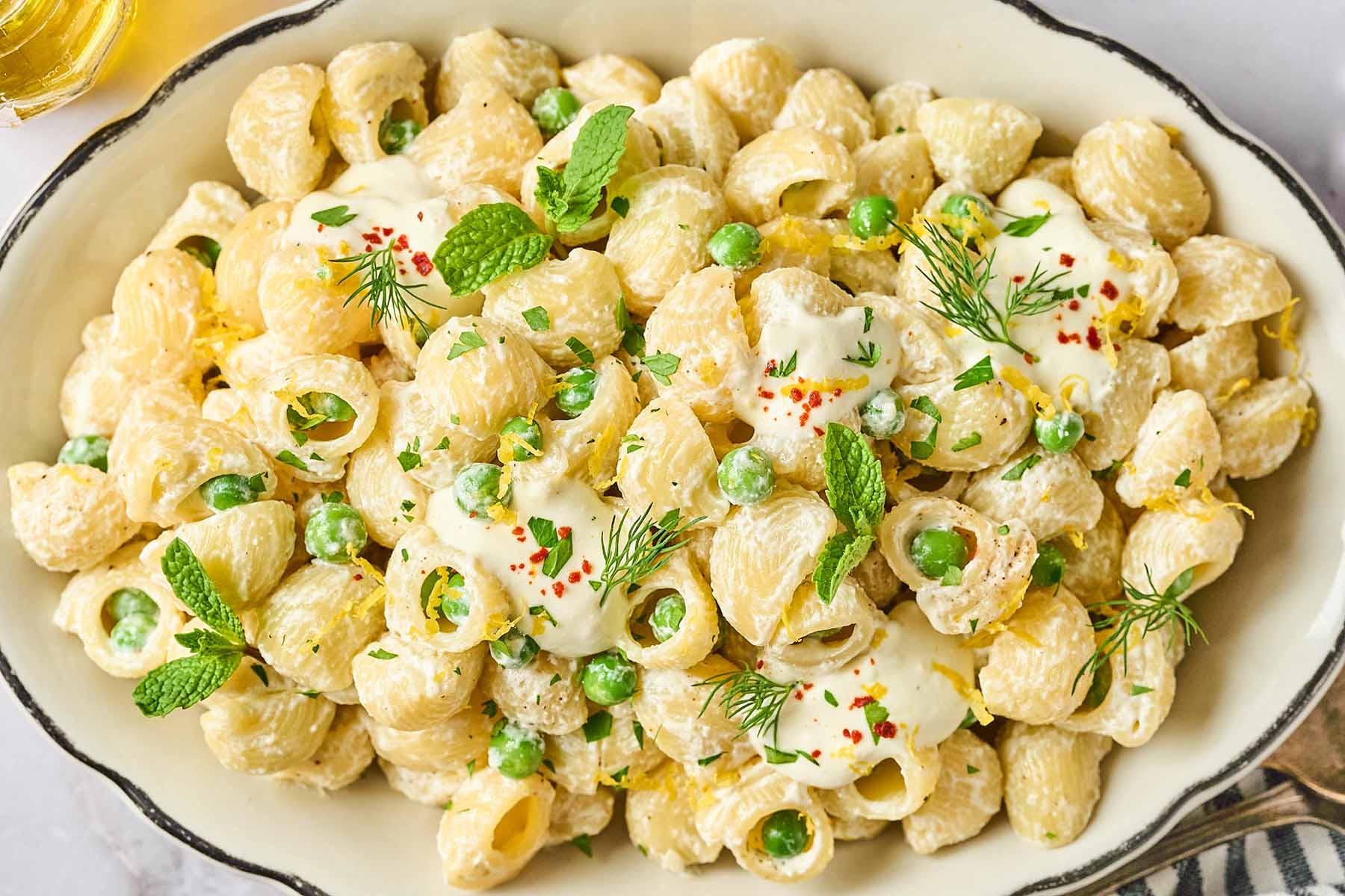 Creamy garlic lemon pasta with peas, garnished with mint, dill, lemon zest, and red pepper flakes, served in a white dish with a rustic black trim.