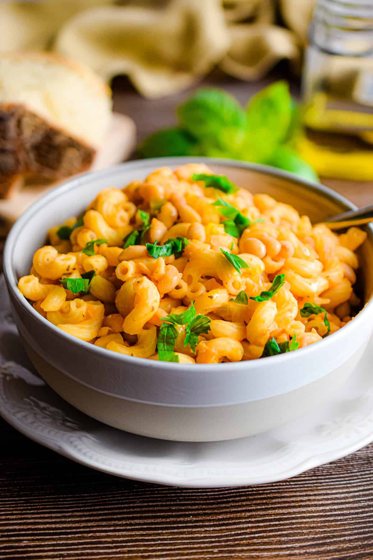 The pasta fagioli is in a bowl surrounded by basil, olive oil, and a yellow napkin.