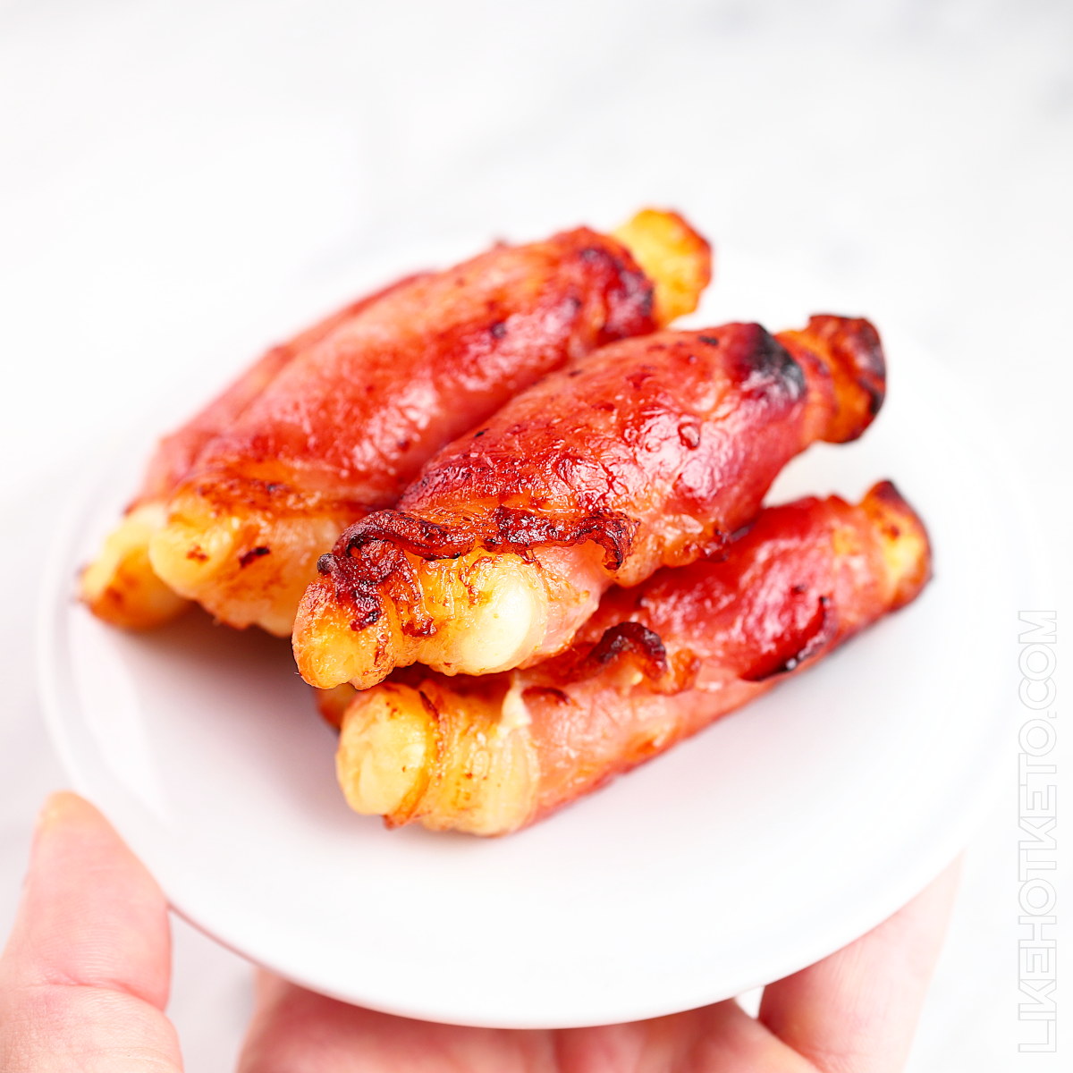 Crunchy bacon wrapped halloumi cheese rolls piled up in a white plate.