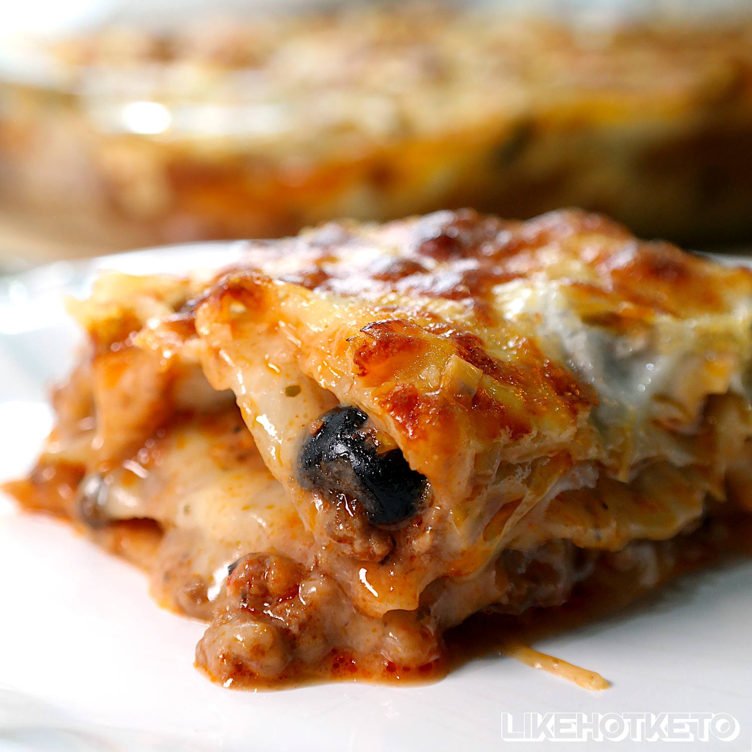 Slice of keto cabbage lasagna with melting mozzarella cheese and a black olive.