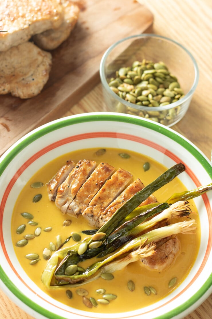 Keep the chill of winter at bay with this hearty Pepita Pork Pumpkin Soup. Creamy pumpkin soup with pan-seared pork loin chops and charred onions, all finished with a sprinkling of toasty pepitas, this soup will warm the body and soul.