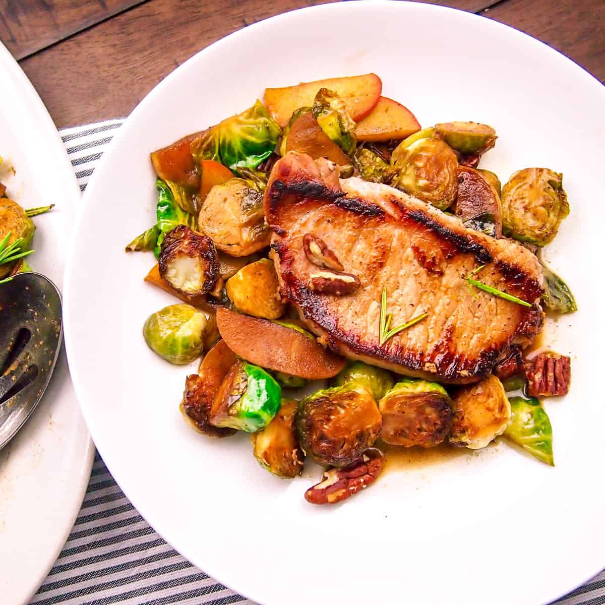 Pork chop on a bed of brussels sprouts and apples on a white plate.