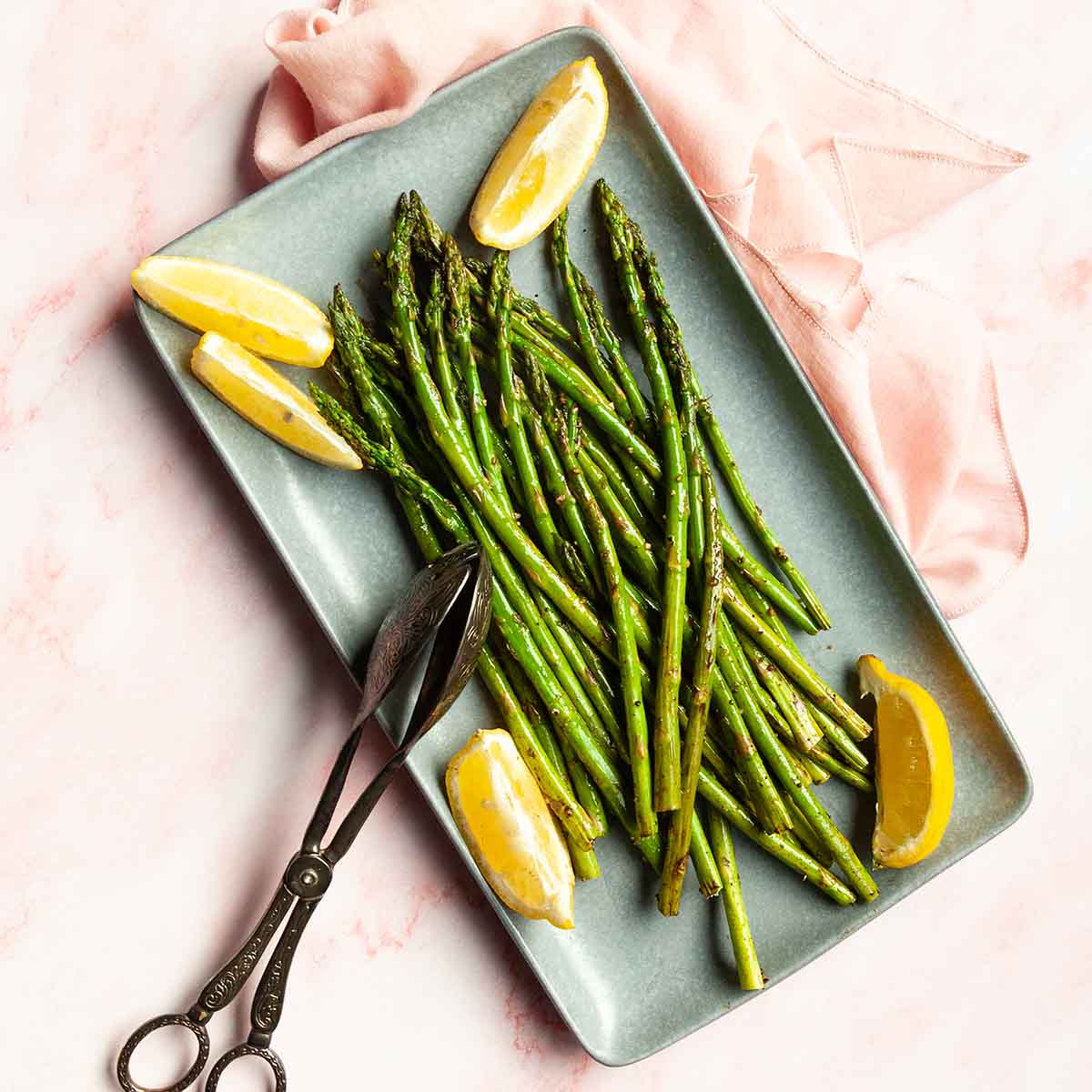 Cooked asparagus on a platter with lemon wedges.