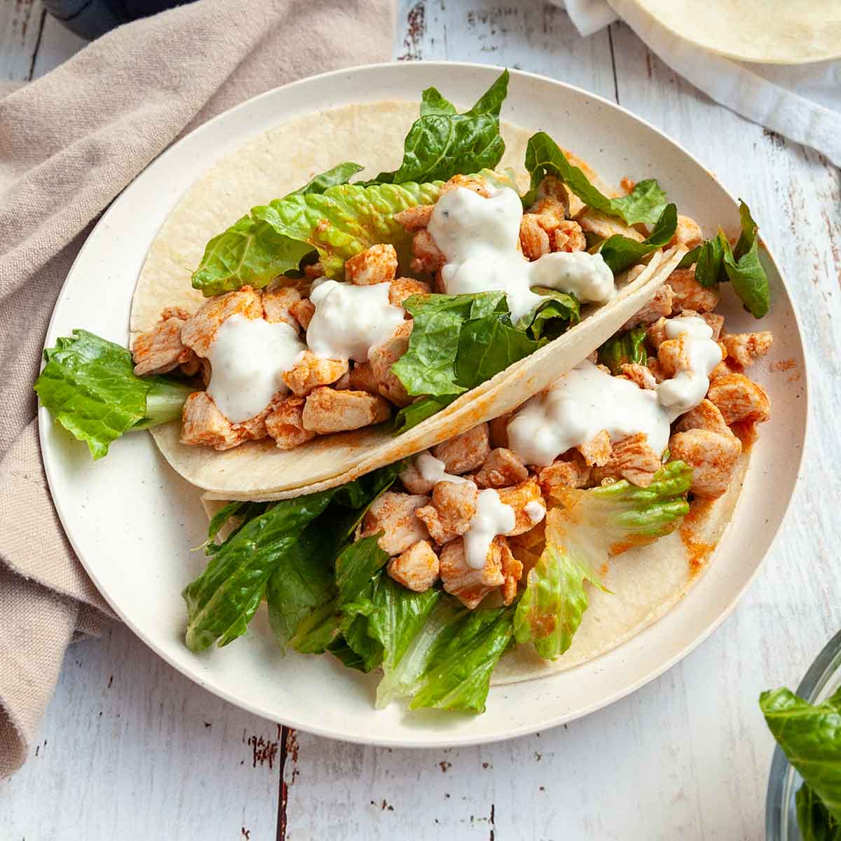 Two Buffalo chicken tacos on a plate with romaine lettuce and blue cheese dressing on top.