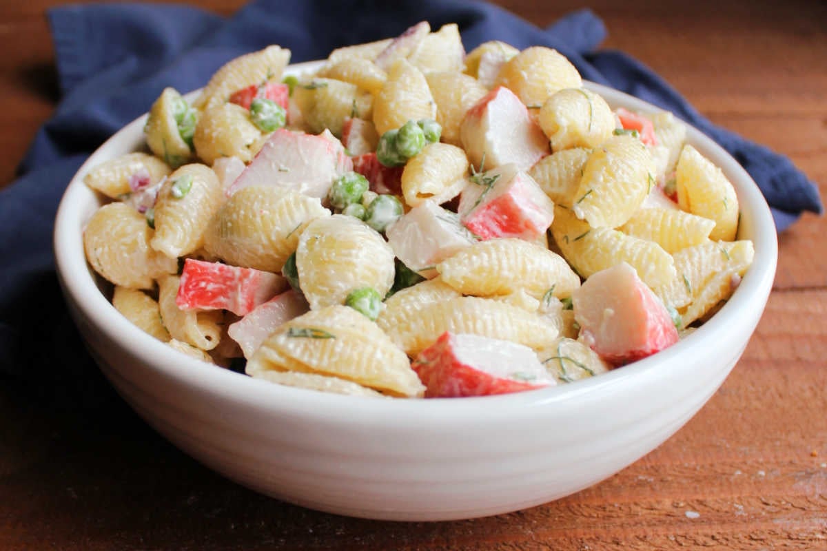 Bowl of imitation crab pasta salad with peas, red onions, shell pasta, and creamy dressing.