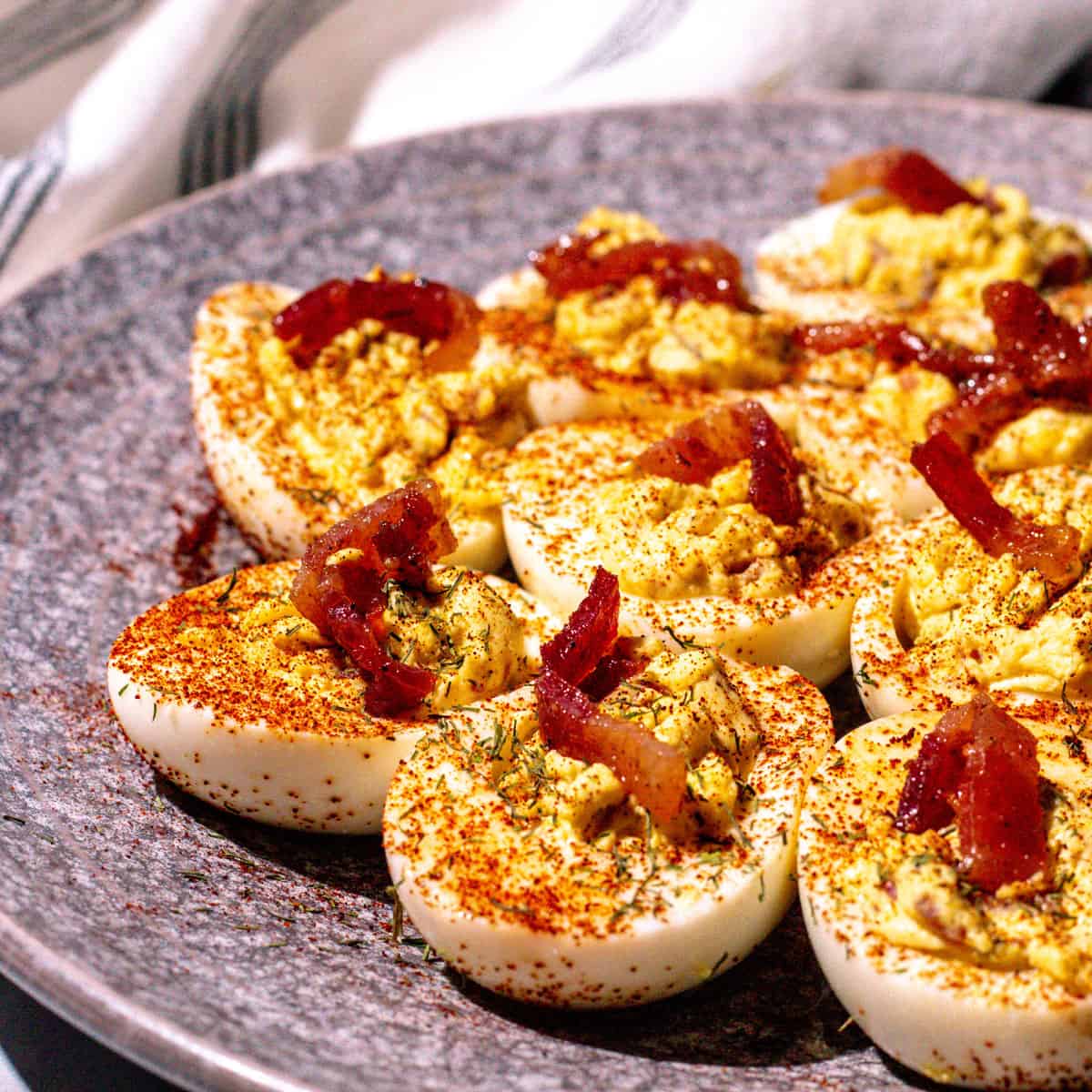 Deviled eggs garnished with crumbled candied bacon, paprika, and dill.