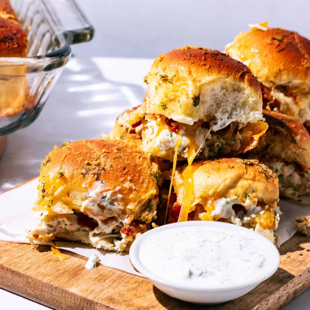The sliders oozing cheese spread out on a wooden platter and a side of ranch dressing.