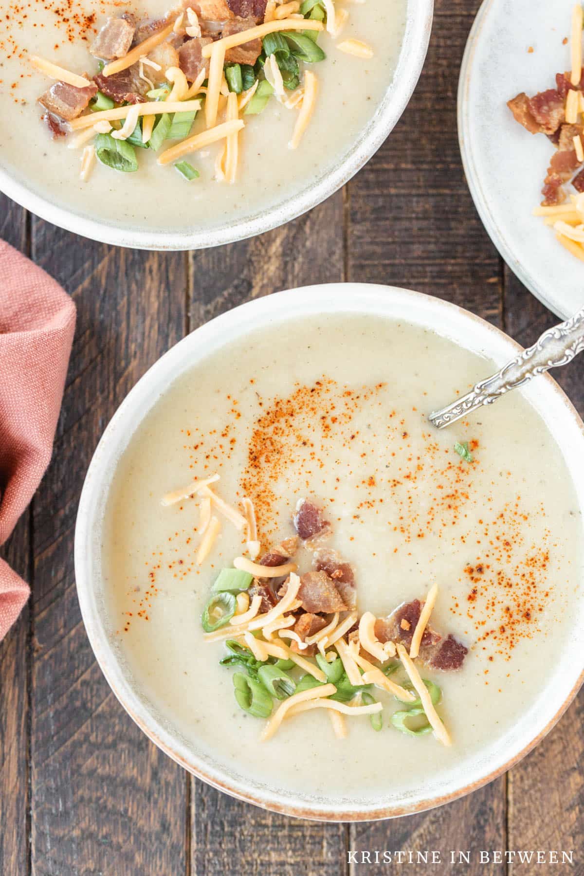 A bowl of cauliflower soup garnished with bacon bits, green onion, and cheese.