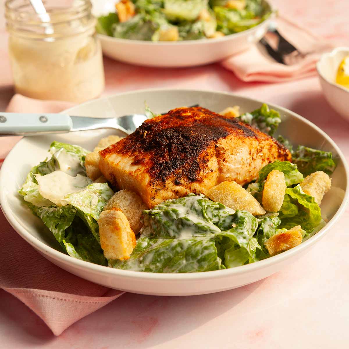 A piece of blackened salmon on a Caesar salad.