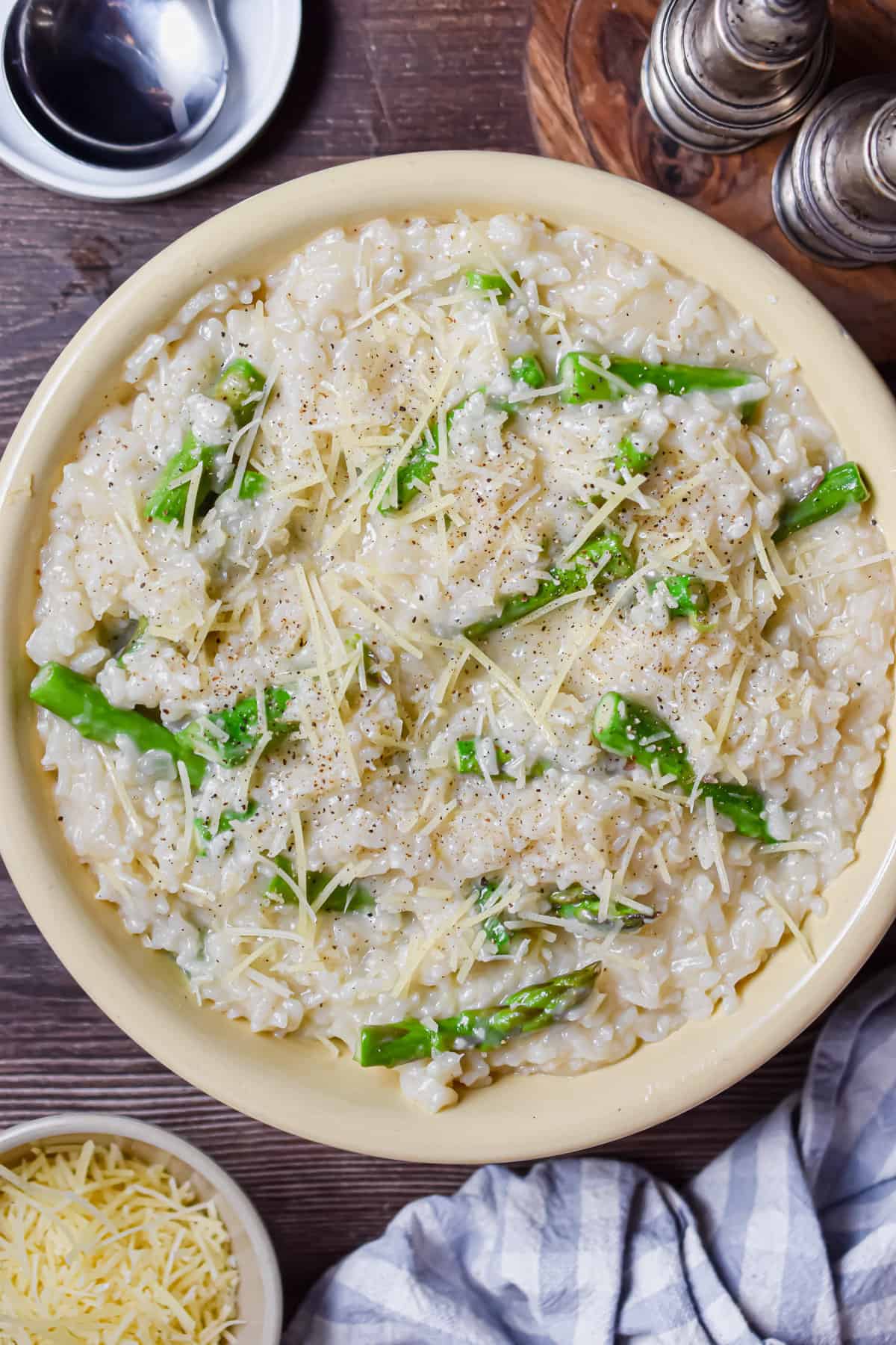 A bowl of Instant Pot Asparagus Risotto is in a bowl surrounded by cheese and a cloth.