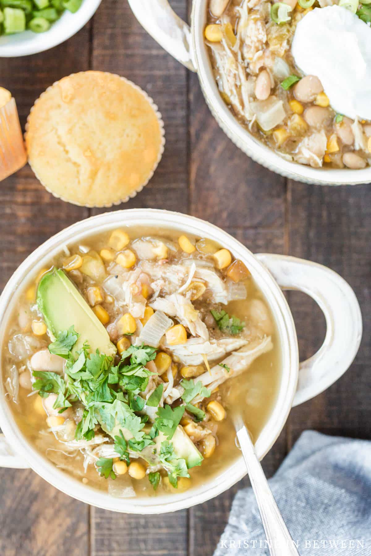 Two bowls of chicken chili garnished with chopped cilantro and avocado sitting with a light blue napkin.