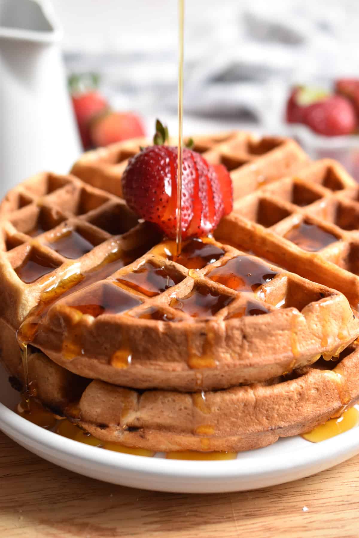 Maple syrup is being poured on a stack of strawberry waffles.
