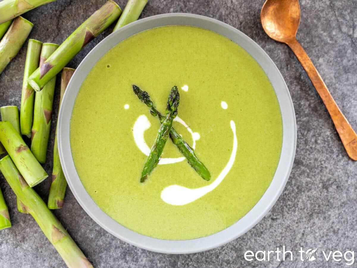 A bowl of cream of asparagus soup drizzled with vegan cream and fresh sauteed asparagus.