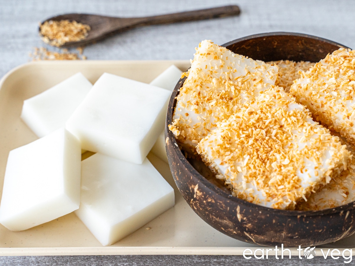 Hawaiian haupia squares on a beige plate, next to a coconut bowl which is filled with haupia coated with toasted coconut.