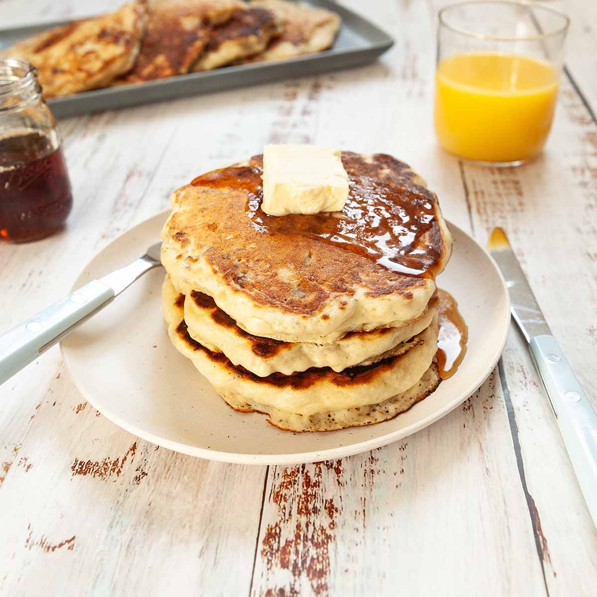 Three pancakes on a plate topped with maple syrup and butter.